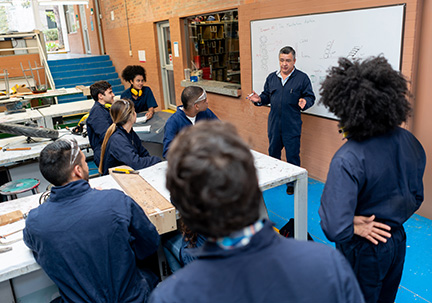 a teacher in a mechanics class is talking to a group of attentive students